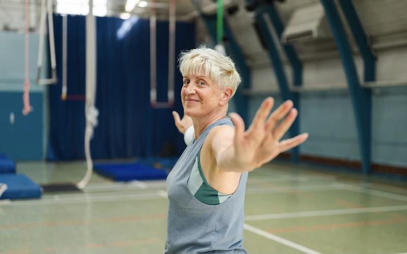 A smiling older woman stretching in a gym