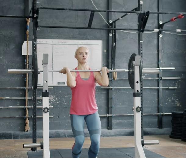 A woman pressing a barbell in a squat rack