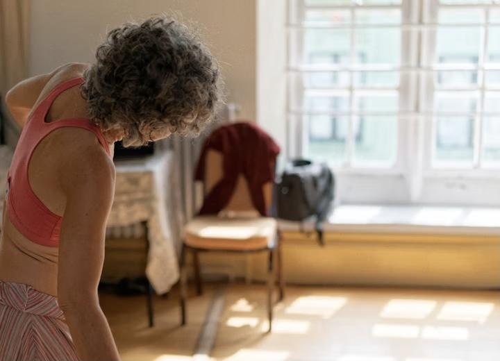 A woman with grey curls stretching in a sunlit room