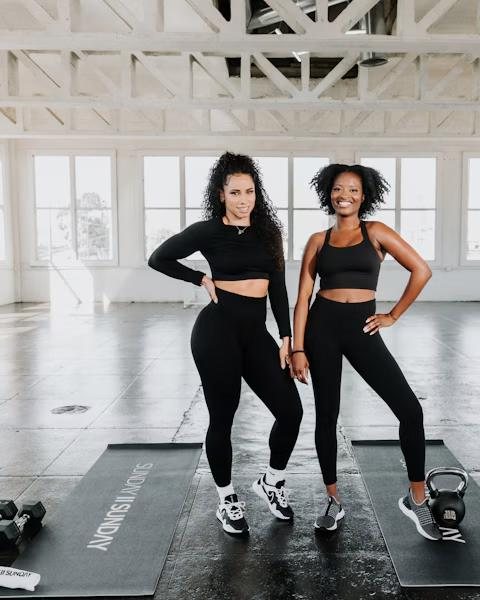 Two women standing together, smiling, in a bright gym
