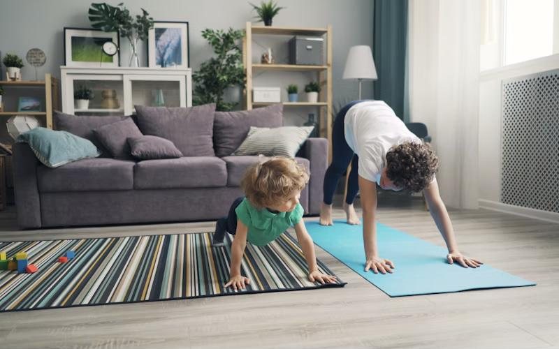 A mum doing a yoga stretch at home while her young child copies her